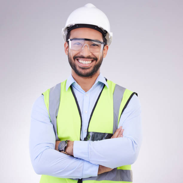 Construction worker in portrait, man with crossed arms and smile, architect or engineer in building industry on studio background. Happy contractor, professional builder with helmet and goggles