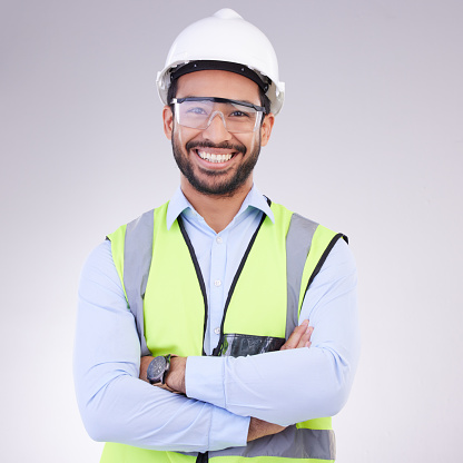 Construction worker in portrait, man with crossed arms and smile, architect or engineer in building industry on studio background. Happy contractor, professional builder with helmet and goggles