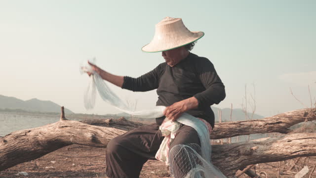 Video footage of Local lifestyles of fisherman fixes holes and tangles in his fishing net.