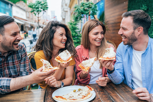 Group of happy young friends eating pizza together, outdoor. Cheerful friends eating pizza, smiling and talking, enjoying the day and have fun. Fast food