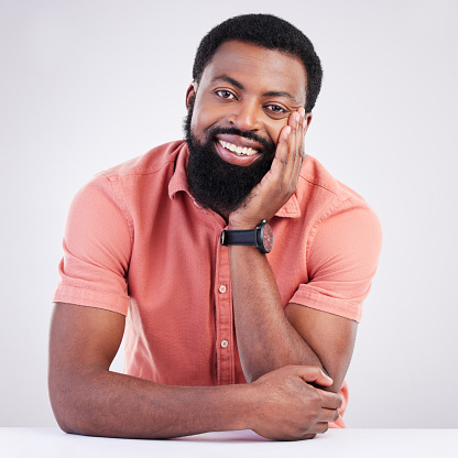 Happy, handsome and portrait of a black man leaning on a table isolated on a white background. Smile, relax and an African guy looking relaxed, calm and at peace with confidence on a studio backdrop