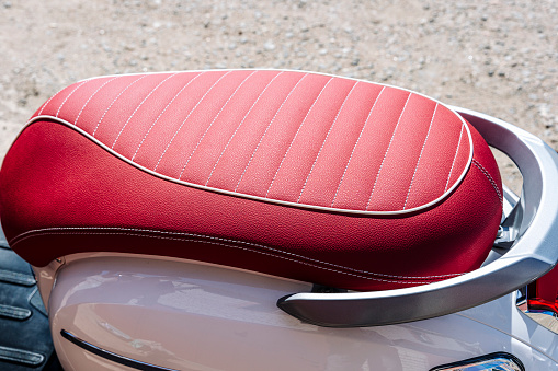 gorgeous red leather motorcycle seat with white stitching. the scooter seat is made of red leather. Part of a motorcycle. background with red leather texture. Texture, artificial leather with stitching