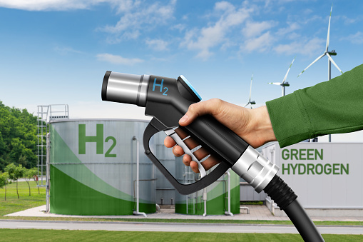 Hand with hydrogen fueling nozzle on a background of H2 factory. Hydrogen production from renewable energy sources concept