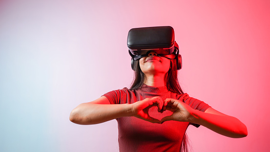 Young Asian Indian woman holding heart-shaped hands, wearing virtual reality headset, a girl with vr glasses concept studio portrait