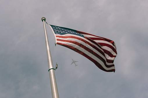 American flag and pole with an airplane flying behind the clouds in the background