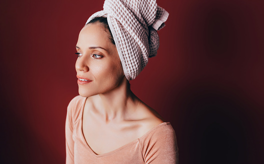 A portrait of a smiling woman with a white towel on her head, looking away.