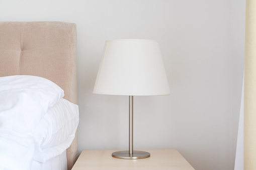 Elegant bedside lamp with white shade on night table in bedroom, selective focus