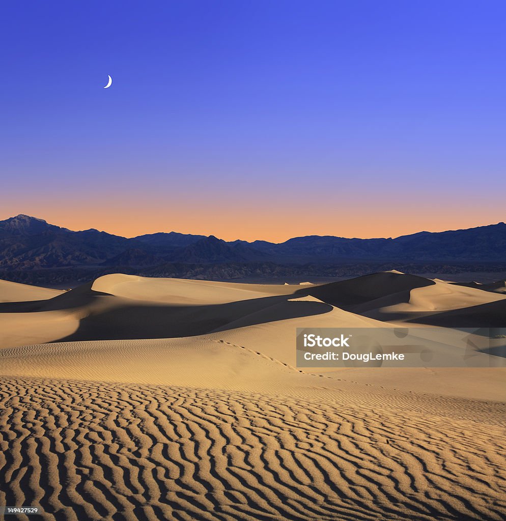 Moon And Dunes Early Morning Sunlight Merges With A Twilight Moon Over Sand Dunes And Mountains At Death Valley National Park, California, USA Stove Pipe Wells Stock Photo