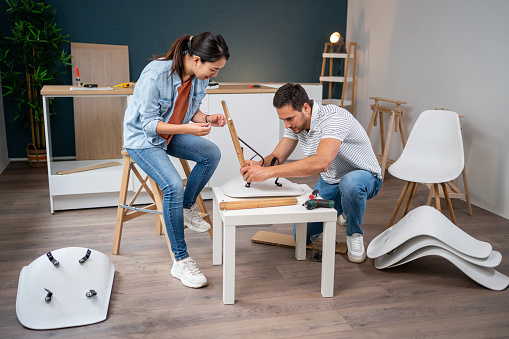 The multiracial couple, a young Caucasian man and a Japanese woman, together assembling trestles on a chair, while using a screwdriver