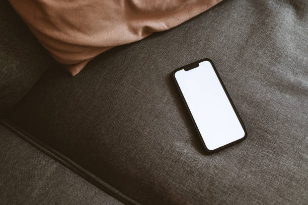 istock Smart mobile phone device with blank white mockup screen on living room sofa 1494276957
