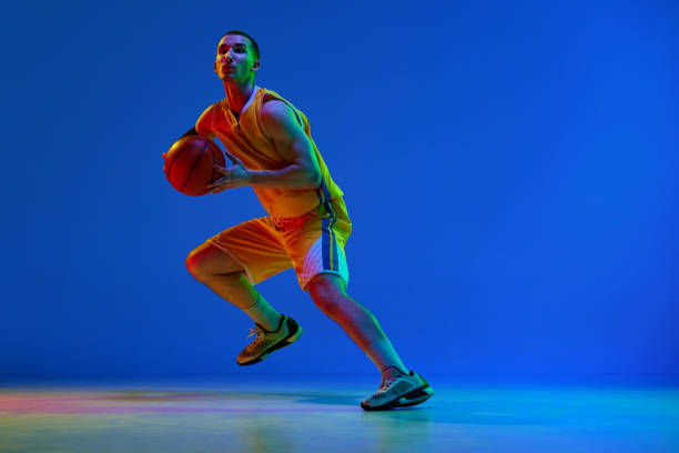 istock Dynamic image of young basketball player in yellow uniform during game, training against blue studio background in neon light. 1494277701