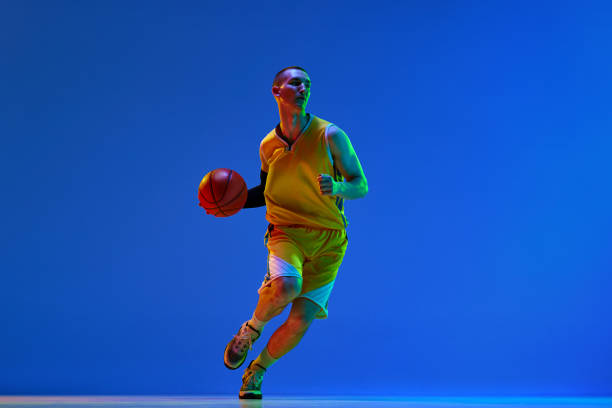 istock Dynamic image of young man, basketball player in motion during game, training against blue studio background in neon light. 1494277749