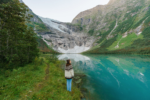 Young Caucasisan woman in knitted sweater standing on the background of Jostedalsbreen  glacier