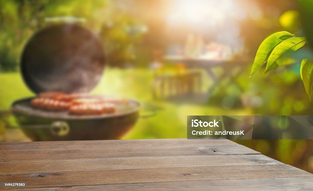 summer time in backyard garden with grill BBQ, wooden table, blurred background Barbecue - Meal Stock Photo