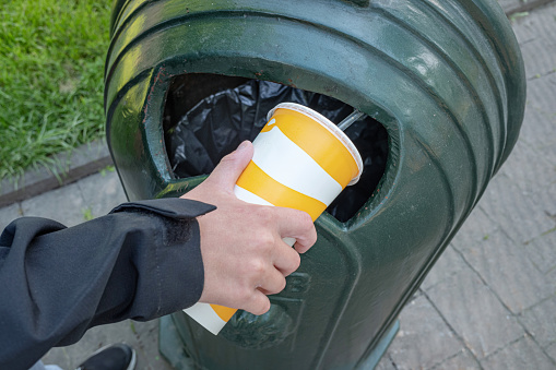Hand throwing empty disposable paper cup drop in recycling bin