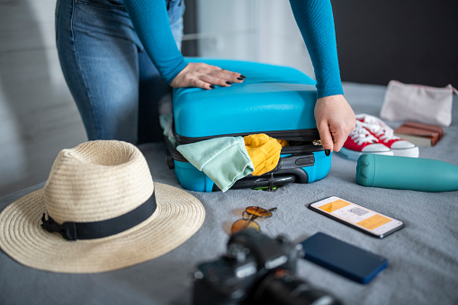 Woman packing luggage for vacation and struggling to close the suitcase.