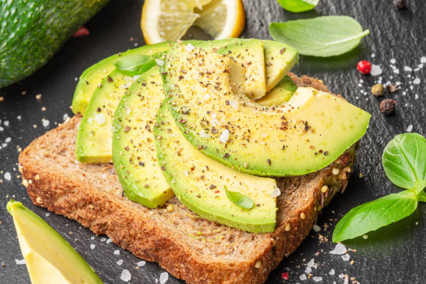 istock Avocado toast - bread with avocado slices on natural slate serving board. Top view. 1494285586