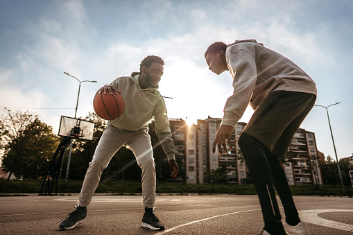 Friends playing one on one basketball on outdoor court