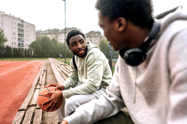 istock Two young friends having casual conversation while sitting on a bench after a basketball game 1494285599