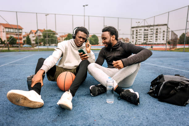 istock Two young friends using phone while sitting on a basketball court after practice 1494285803