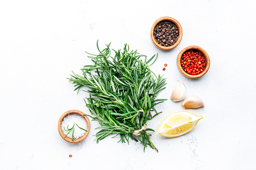Fresh rosemary, sea salt, black and pink pepper, garlic and olive oil on white kitchen table background. Spices and herbs for cooking. Top view