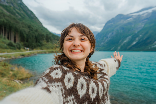 Selfie of  young Caucasian woman in sweater on the background of lake in Norway