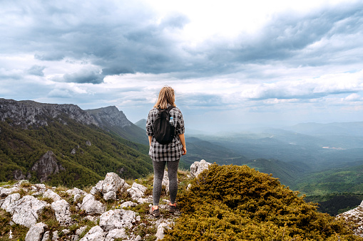 Rear view of casually clothed female hiker enjoying a view while standing on the top of the mountain