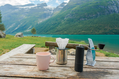 Coffee grinder, pour over and pack of coffee beans on the table on the background of blue lake