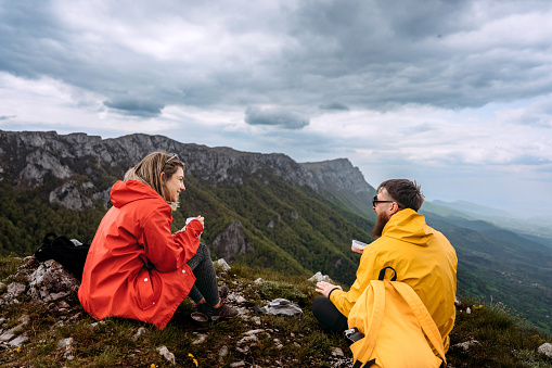 Two hikers on top of the mountain enjoying breakfast while sitting on the rock on the top of the mountain