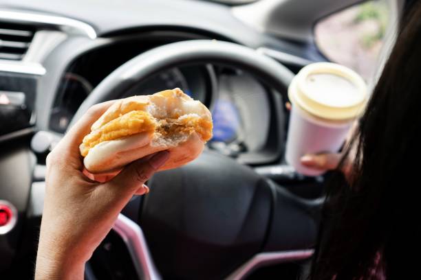 primer plano de la mano de la mujer sosteniendo hamburguesas y café, comiendo y bebiendo mientras conduce el automóvil - driving car distracted accident fotografías e imágenes de stock