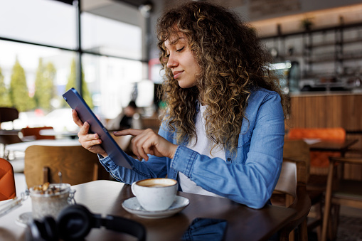 Young smiling woman using digital tablet and enjoying coffee drink at a cafe