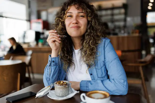 Photo of Smiling young woman eating chia pudding for breakfast at cafe