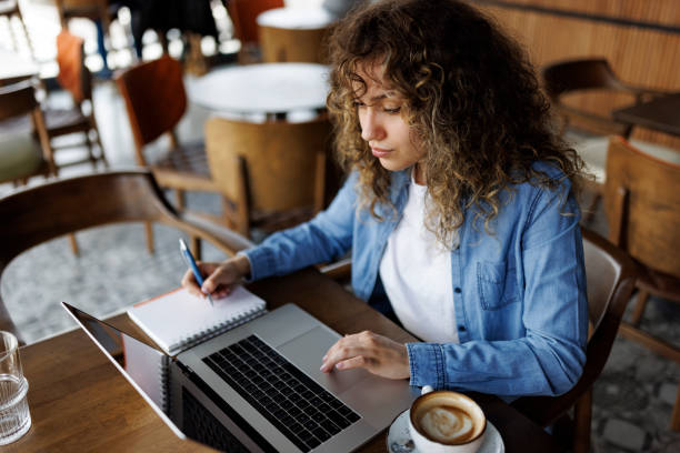 istock Attractive young woman working on laptop and taking notes at a cafe 1494296157