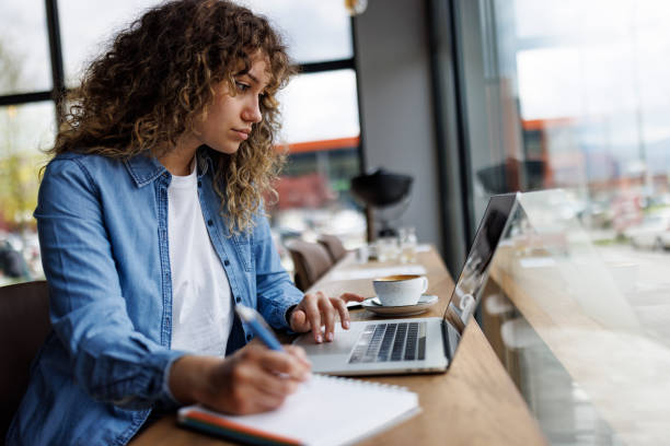 istock Attractive young woman working on laptop and taking notes at a cafe 1494296499