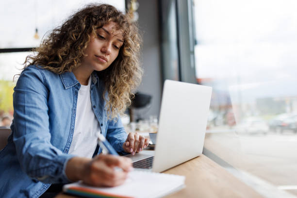 istock Young woman working on laptop and taking notes at a cafe 1494296505