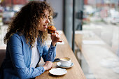 Young woman eating muffin and drinking coffee at a cafe