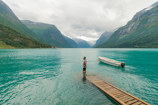 Young Caucasian man standing near the turquoise  lake in Norway