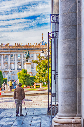 Madrid Palacio Real seen on a sunny winter day with an old man walking next to the columns of an adjacent building