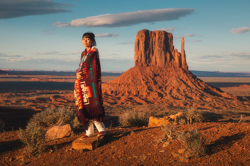 A Navajo teenage girl poses for a portrait in front of famous West Mitten in the Monument Valley Tribal Park, Arizona.