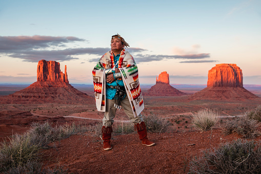 Portrait of a Navajo man wrapped in a Navajo blanket standing in front of the famous Monument Valley view in Arizona/Utah.