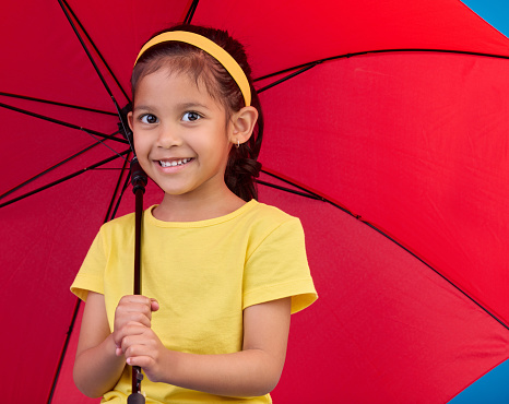 Winter, happy and portrait of a child with an umbrella isolated on a blue background in a studio. Smile, safety and a young girl holding a tool to protect from rain, bad weather and the cold