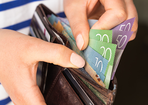 A woman taking New Zealand banknotes from a leather wallet to pay with.