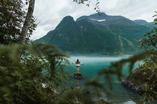 Mysterious view of woman in knitted sweater standing on the rock in the lake covered with fog