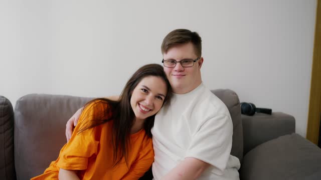 Young man with Down syndrome with his female friend embracing sit on sofa