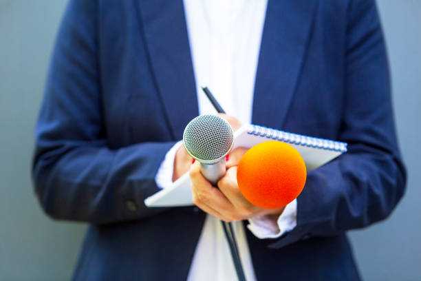 News reporter at media event or press conference, holding microphone, writing notes. Broadcast journalism concept. stock photo