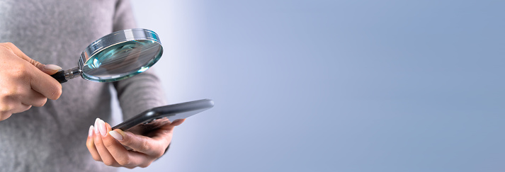 Young woman looks at the phone with a magnifying glass