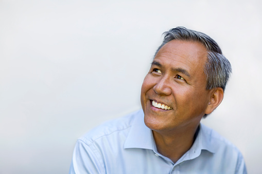 Portrait of Asian Chinese mixed race senior mature man in collared business shirt smiling looking upward