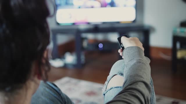 Woman changing channels while watching tv in her living room at home
