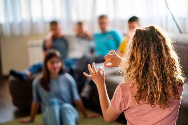 Rear view of group of children playing charades at home Group of teenagers playing at home. Children playing charades pantomime stock pictures, royalty-free photos & images