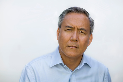 Portrait of Asian Chinese mixed race senior mature man in collared business shirt making a confused face looking at camera